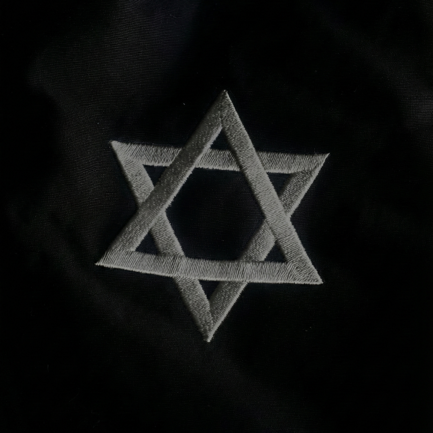 A close-up of a black embroidered star of David on a black fabric.