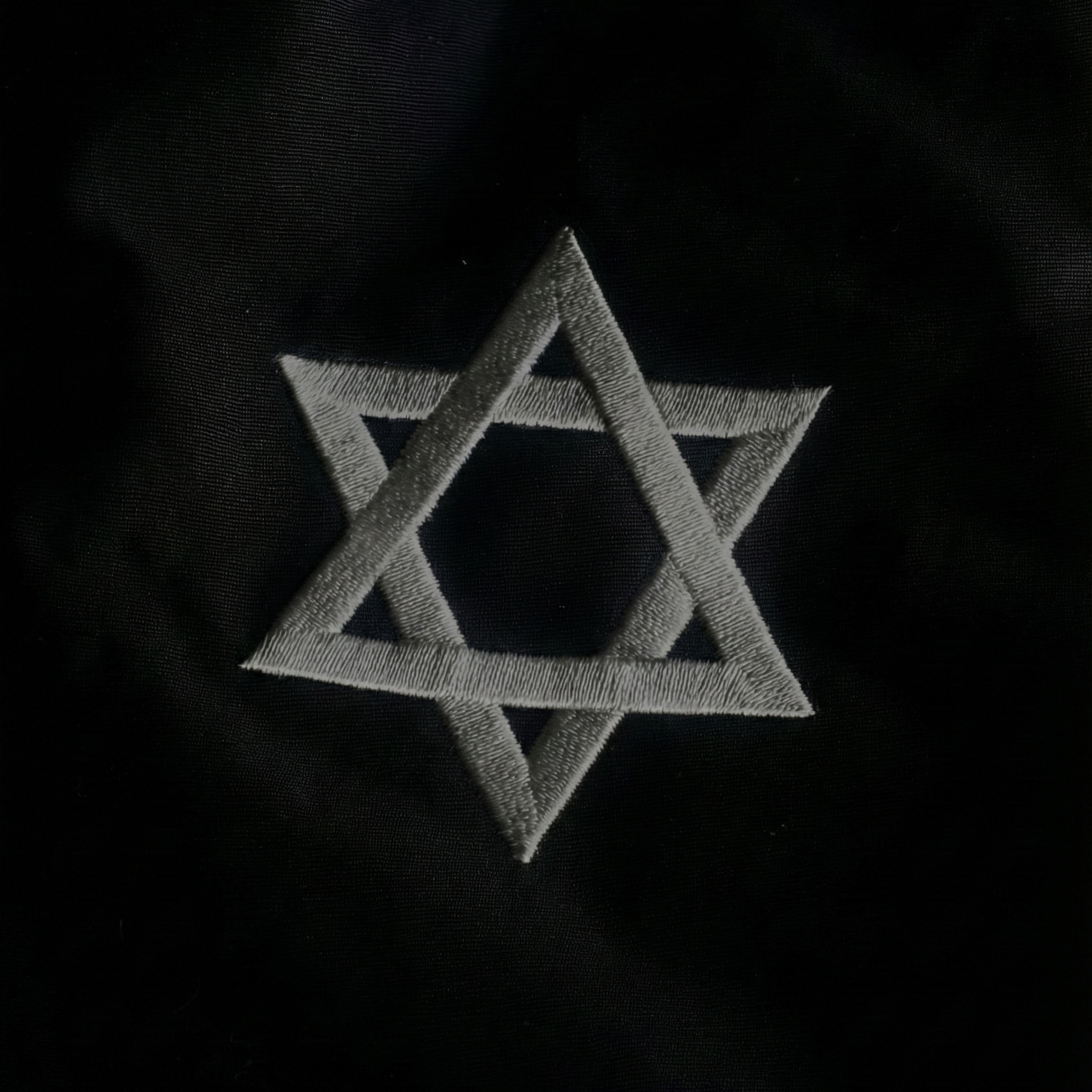 A close-up of a black embroidered star of David on a black fabric.