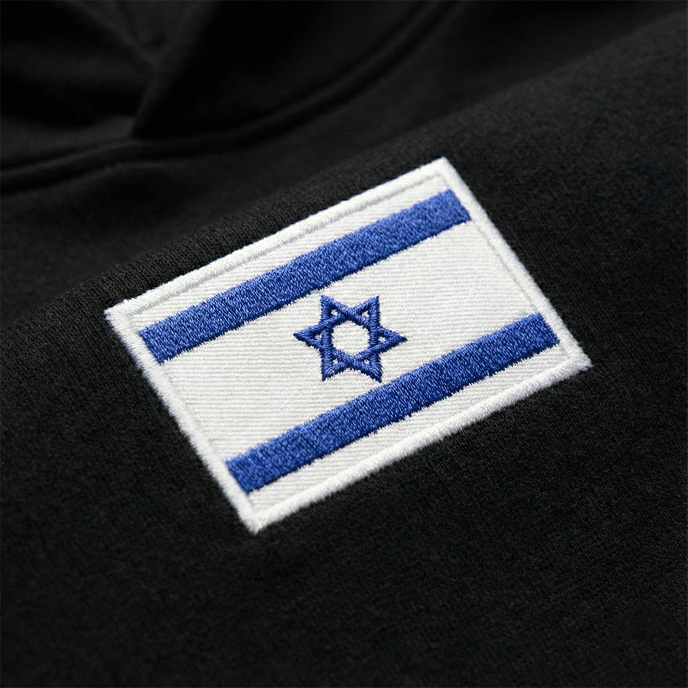 A close-up of an embroidered Israeli flag patch on a black sweatshirt.